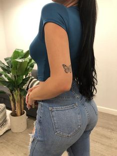 a woman with long black hair wearing blue jeans and a butterfly tattoo on her arm