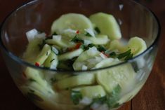 a glass bowl filled with cucumber and other veggies on top of a wooden table