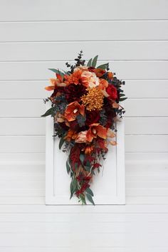 an orange and red wreath hanging on the side of a white building with flowers in it