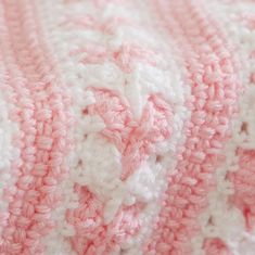 a pink and white crocheted blanket laying on top of a bed