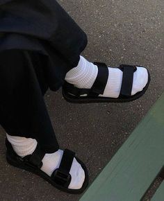 a person sitting on a bench wearing black and white shoes with straps around their ankles