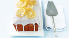 a white plate topped with cake covered in lemon slices next to a knife and fork