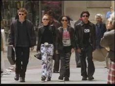 several people walking down the street with one person wearing sunglasses and another in a black jacket