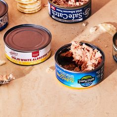 three tins of food sitting on top of a table next to some crackers