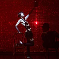 a woman standing on top of a chair in front of a red wall with lights