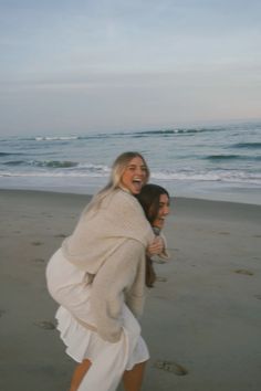 two women are hugging on the beach by the water's edge while one woman is holding her back