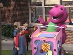 children are standing in front of a large purple toy dinosaur on the lawn with other kids