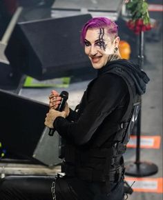 a man with purple hair and makeup holding a microphone