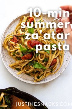 a white plate topped with pasta covered in tomatoes and spinach next to a hand holding a fork