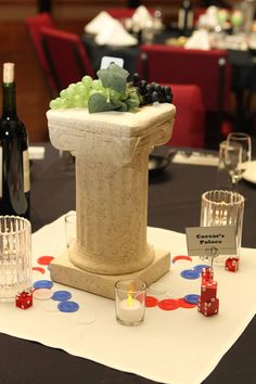 a table topped with a vase filled with grapes and other items next to wine glasses