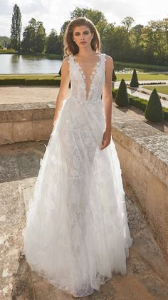 a woman in a white wedding dress standing on the steps near some water and trees