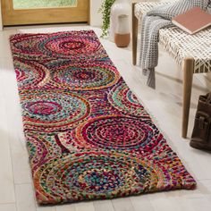 a multicolored area rug on the floor in front of a chair and window