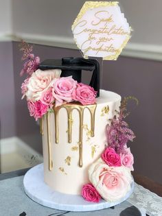 a white and gold cake with pink flowers on the top, topped with a sign that says congratulations to your special occasion