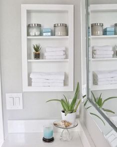 a white bathroom with shelves filled with towels and plants on the counter top next to a mirror