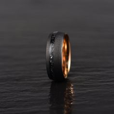 a black and gold wedding band with an etched design on the inside, sitting on a dark surface