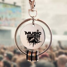 a keychain hanging from a metal ring with music festival logo on it and people in the background