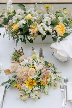 the table is set with white and yellow flowers in vases, napkins and silverware