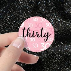 a hand holding a pink sticker with the word thirty printed on it