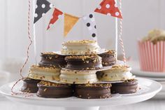 a white cake plate topped with chocolate covered donuts and cupcakes next to flags