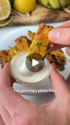 a person dipping some food into a small bowl with ranch dressing on it and lemons in the background