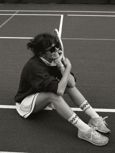 a young woman sitting on top of a tennis court holding a racquet