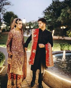 a man and woman standing next to each other in front of a fountain at night