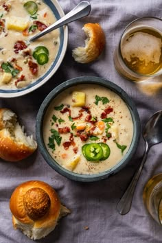 two bowls filled with soup next to rolls on a cloth covered table and spoons