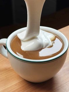 a spoon pouring milk into a cup of liquid on top of a wooden countertop