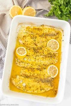 baked fish with lemons and herbs in a white casserole dish