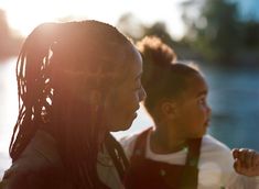 two young women standing next to each other on a river bank with the sun behind them