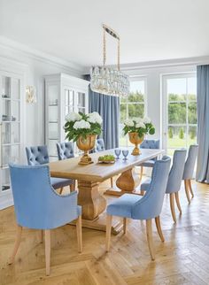 a dining room table with blue chairs and vases on top of it in front of windows