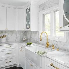 a kitchen with white cabinets and marble counter tops, gold faucets on the sink