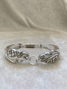 a silver bracelet with an intricate design on the front and back side, sitting on a white cloth