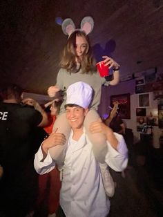 a woman is carrying a man dressed as mickey mouse at a party with other people in the background