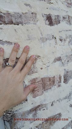 a person's hand on the side of a brick wall with their fingers touching it