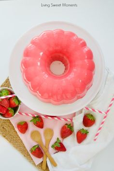 a pink frosted donut sitting on top of a white plate next to strawberries