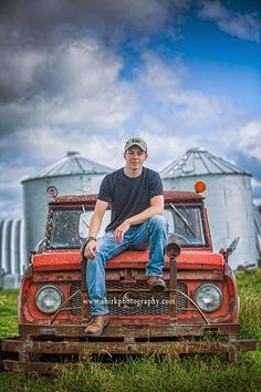 a man sitting on the hood of an old red truck in front of a silo