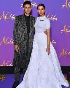 two people standing next to each other in front of a purple wall with the words alada on it