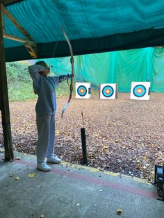 the man is practicing his archery skills at the target practice area in front of the green tarp