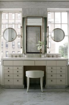 a bathroom vanity with two mirrors above it and a stool in front of the mirror