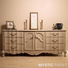 an antique dresser is painted beige with gold trim and ornate carvings on the top, along with two framed pictures