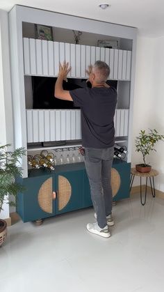 a man standing in front of a tv on top of a blue entertainment center next to potted plants