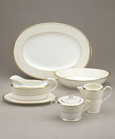 a white and gold dinnerware set with matching saucers, cups, and spoons