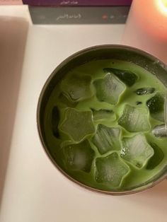 a cup filled with green liquid next to a lit candle