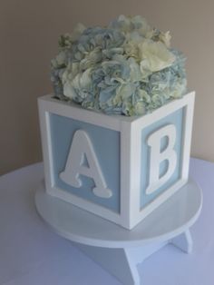 a white and blue cake with the letter a on it's side, decorated with hydrangeas