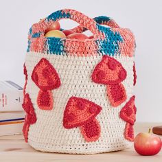 a crocheted basket sitting on top of a wooden table next to an apple