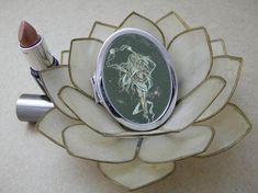 a metal container with a lipstick in it on top of a flower shaped object that is sitting on a table