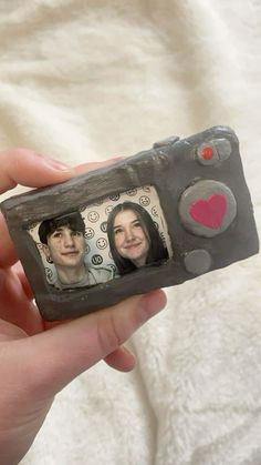 a hand holding a small photo frame with two people on it and a heart in the middle