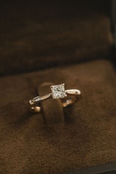 an engagement ring sitting on top of a brown velvet box with a diamond in it