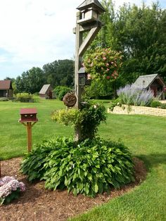 a mailbox in the middle of a garden with flowers around it and a birdhouse on top